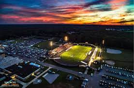 An aerial photograph of the Community Football Stadium in Bedford, Michigan taken at night before the sun is fully set. Bedford, Michigan is a location served by Holland Movers.